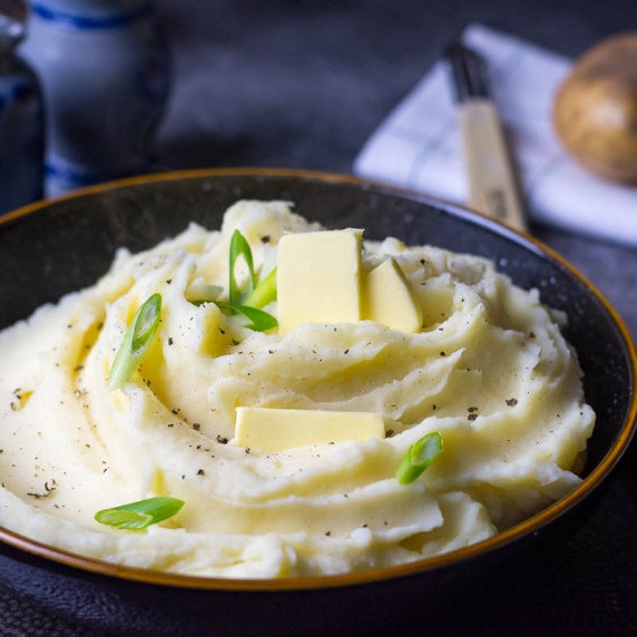 Mashed potato with butter and spring onion on top in a black bowl.
