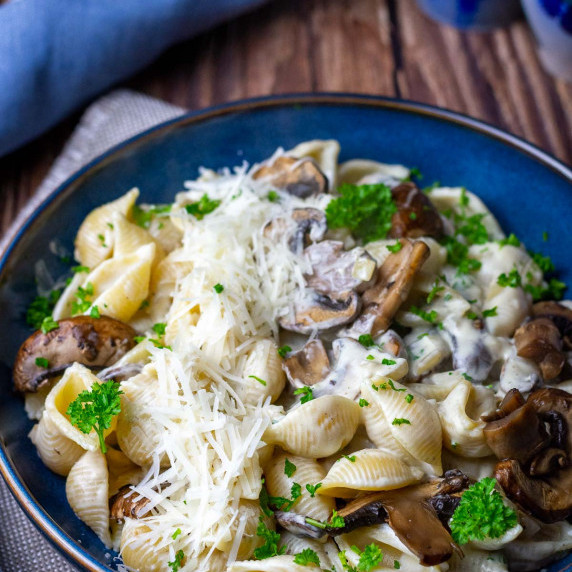 cream cheese pasta with mushrooms in a large blue bowl garnished with parsley. 