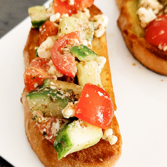 These Greek Salad with Feta cheese Bruschetta are placed on a whte rectangle serving dish.  