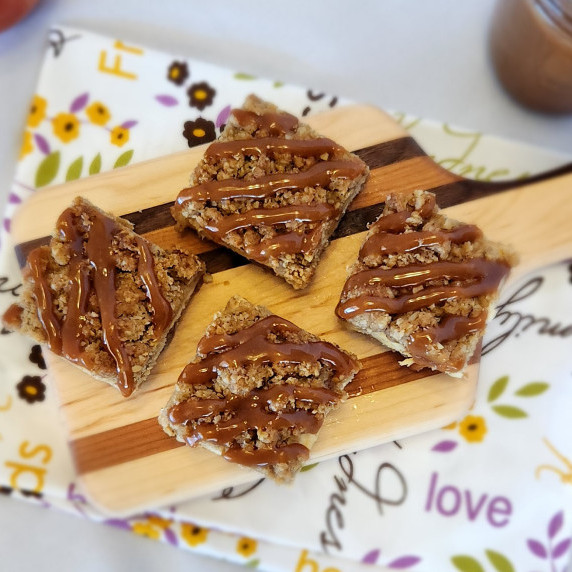 Caramel Apple Cheesecake Cookie Bars arranged on a wooden cutting board against a fabric background