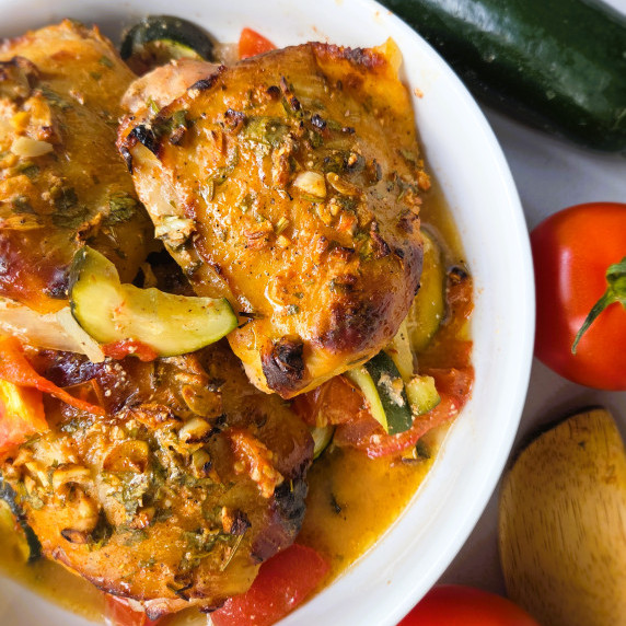 over roasted yogurt-marinated chicken thighs plated with roasted tomatoes and zucchinis