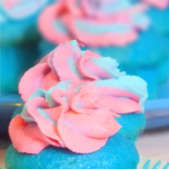 Blue raspberry cupcakes on a blue plate on a white tablecloth.  