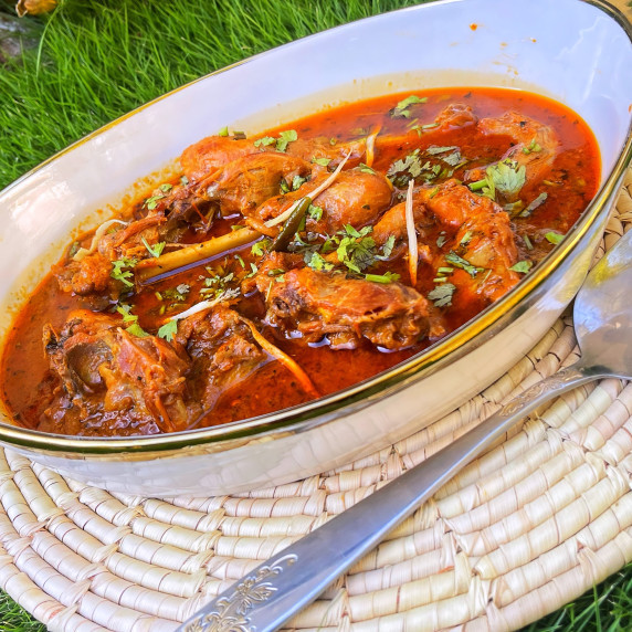 Desi chicken curry arranged in white dish on grass