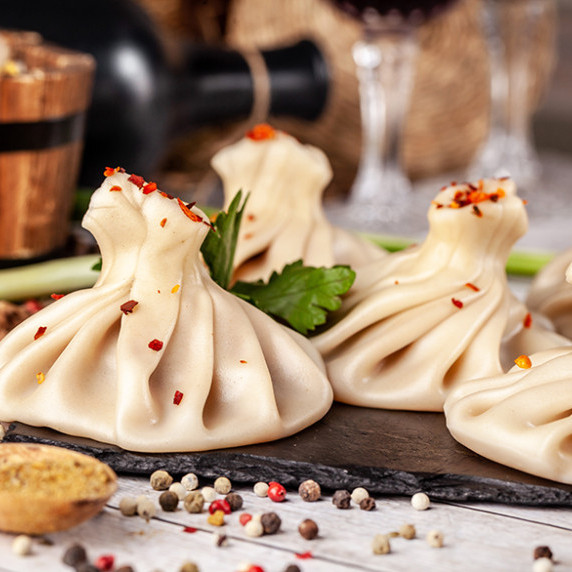 A close-up of several Khinkali, traditional Georgian dumplings, elegantly arranged on a slate board.