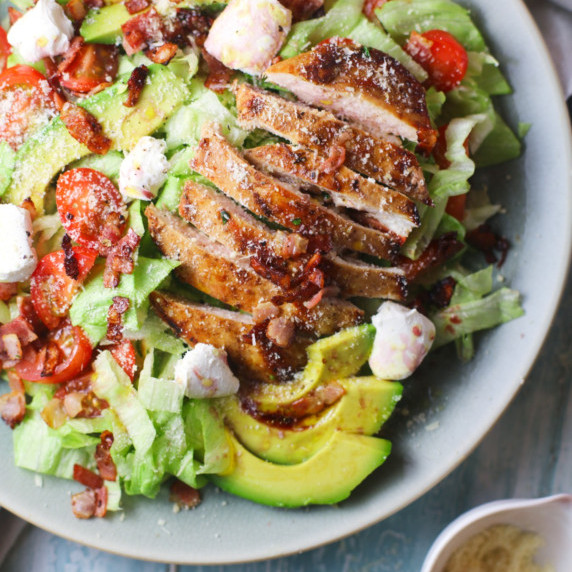Sliced grilled chicken, cubed avocado,sliced cherry tomatoes and salad greens in a white bowl 