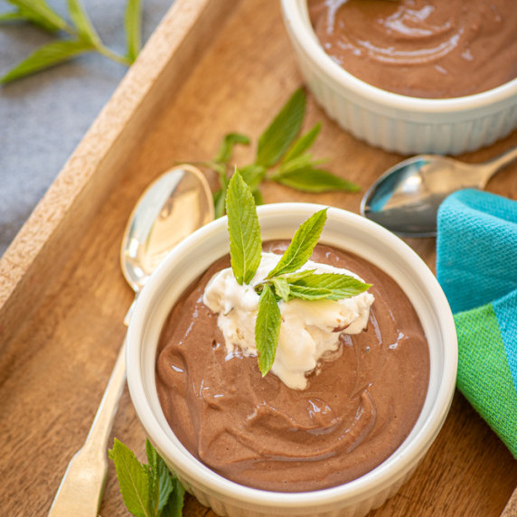 Chocolate pudding topped with coconut whip and a sprig of mint on a wooden tray.