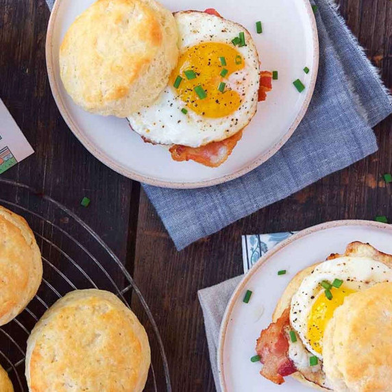 Biscuits on a wire rack next to plated fried egg biscuit sandwiches 
