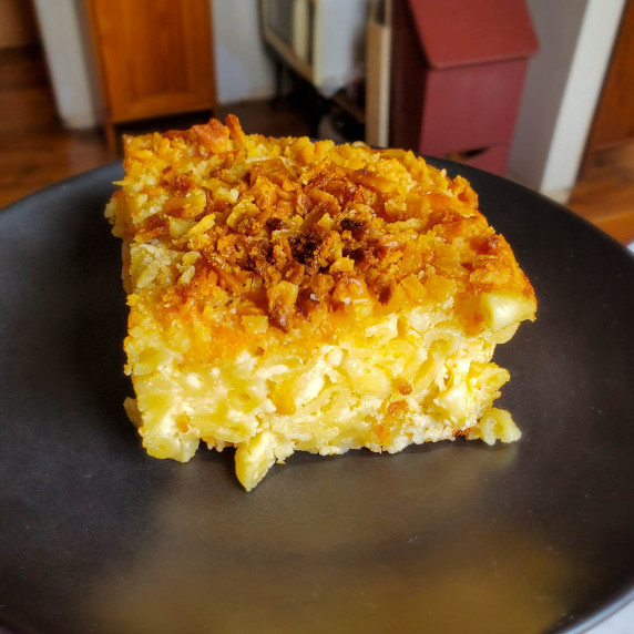 A cheesy slice of baked mac served on a black plate.