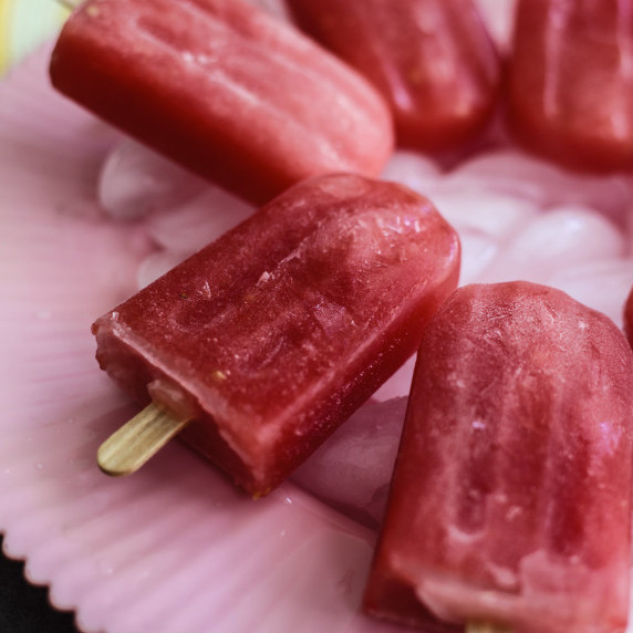 Homemade watermelon and mint popsicles stacked on a plate with fresh mint leaves and watermelon slic