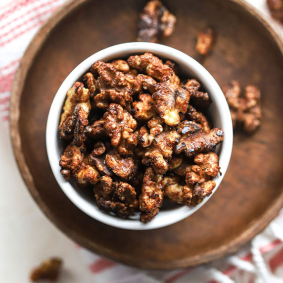 Maple cayenne toasted walnuts in small white bowl on small wooden plate