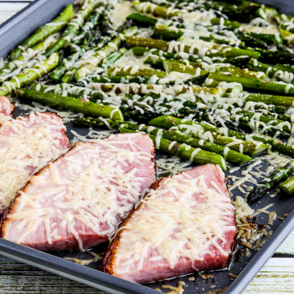 Sheet pan meal with thick slices of ham and roasted asparagus, with melted Parmesan cheese.