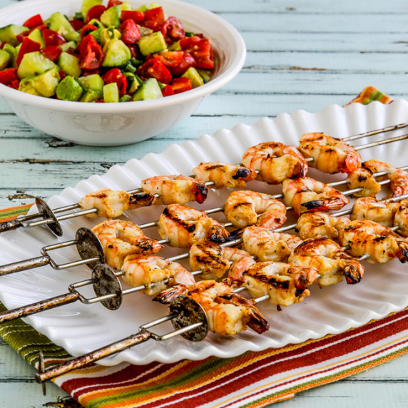 Grilled Shrimp Skewers on serving plate with tomato-avocado salsa in background.