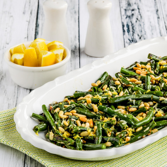 Green Beans with Lemon, Parmesan, and Pine Nuts on serving dish with lemons and salt and pepper