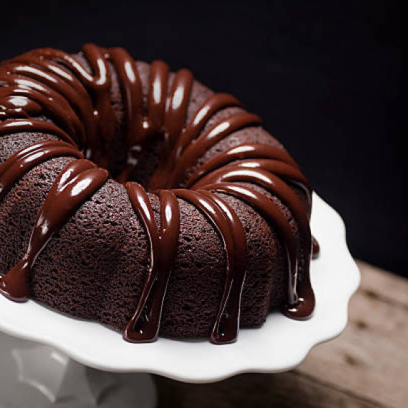 Chocolate bundt cake with chocolate icing on a white cake stand