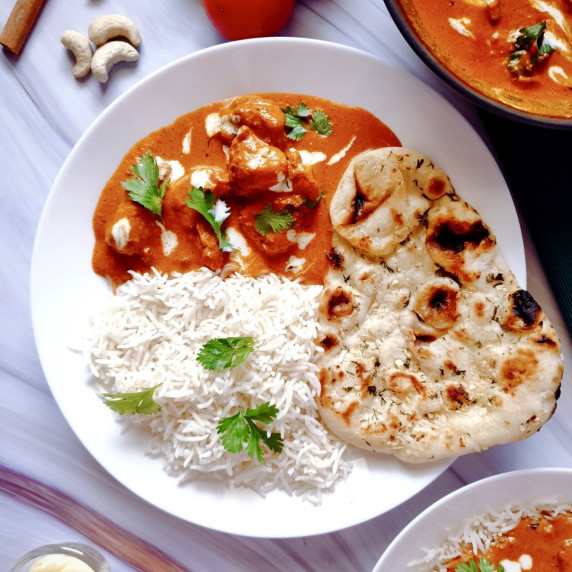 Butter chicken curry in a white plate with butter naan and white rice.