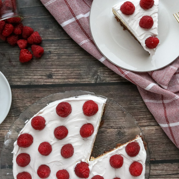 Top view of cheesecake topped with fresh strawberries next to a single slice on a red towel