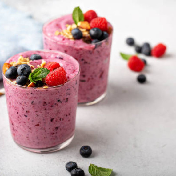 Mixed berry smoothies in glass with fresh berries, granola, and mint sprig