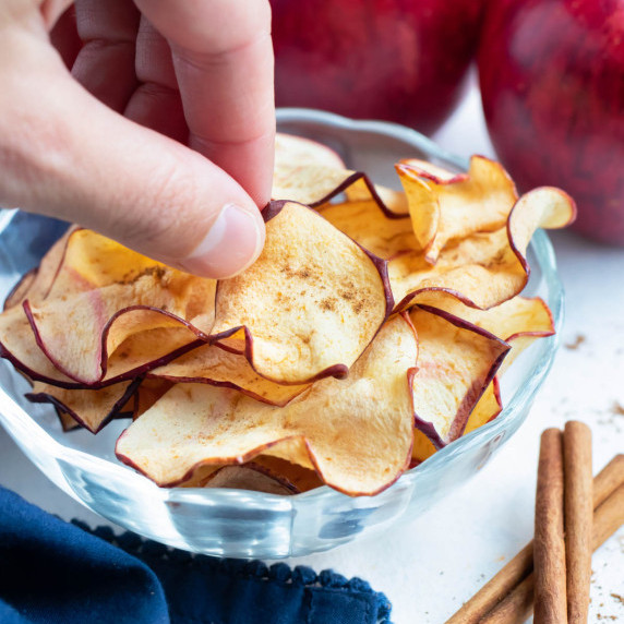 Air Fryer Apple Chips RECIPE served in a white glass bowl and cinnamon sticks. 