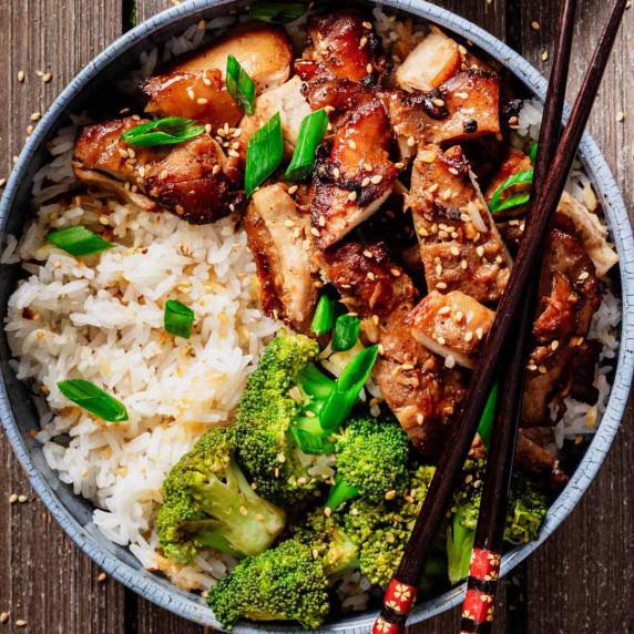 Bowl filled with sliced teriyaki chicken thighs, steamed white rice, and broccoli.