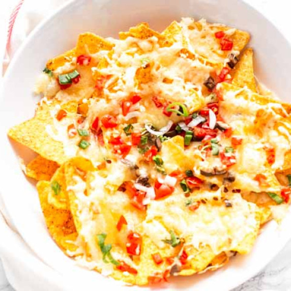Air Fryer Nachos stacked on a plate covered with cheese, tomatoes, olives and more