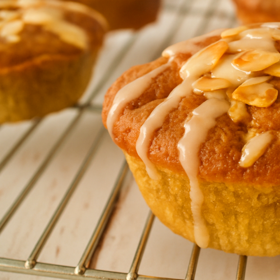 Close-up of almond pear yogurt muffin topped with slivered almonds and drizzles of glaze.