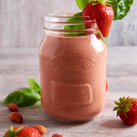 A jar of creamy Almond Strawberry Vinaigrette topped with fresh strawberry and basil