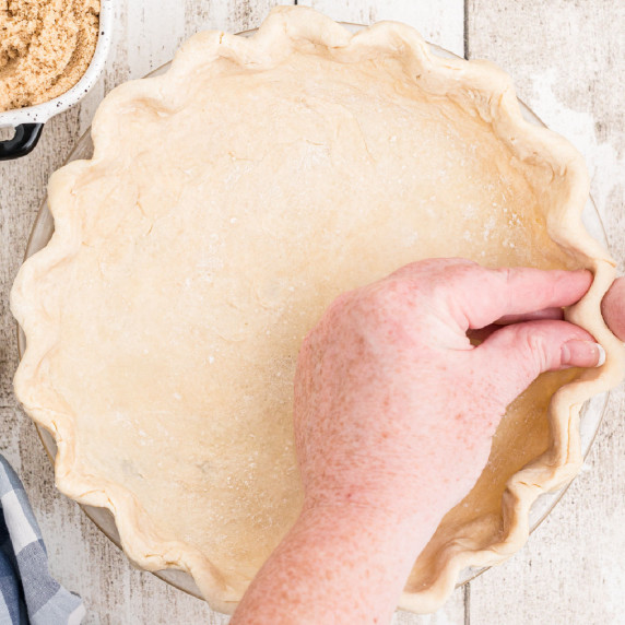 A set of hands fluting the edges of a pie crust.