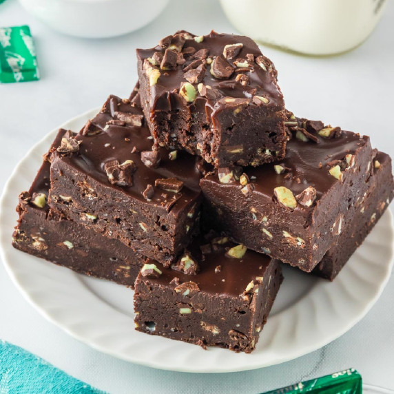 A serving plate with a stack of Andes mint brownies topped with frosting and Andes Mint pieces.