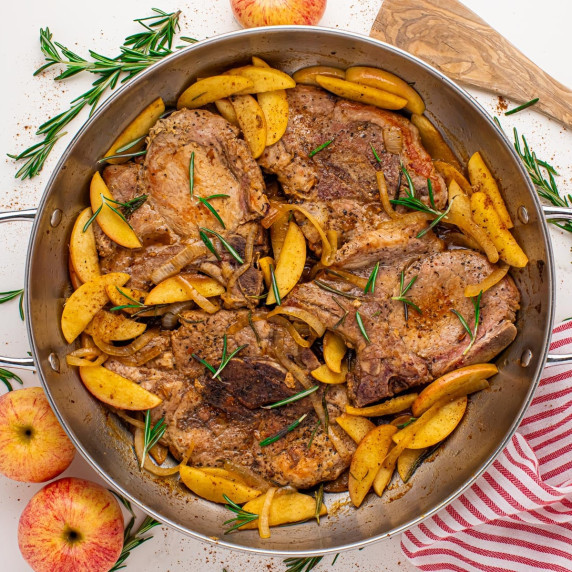 Pan-seared pork chops with apple butter & cooked apples, garnished with rosemary in a large skillet.