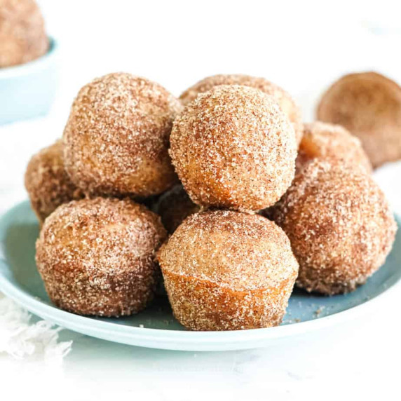 A stack of doughnut holes covered in cinnamon sugar on a plate from the side.