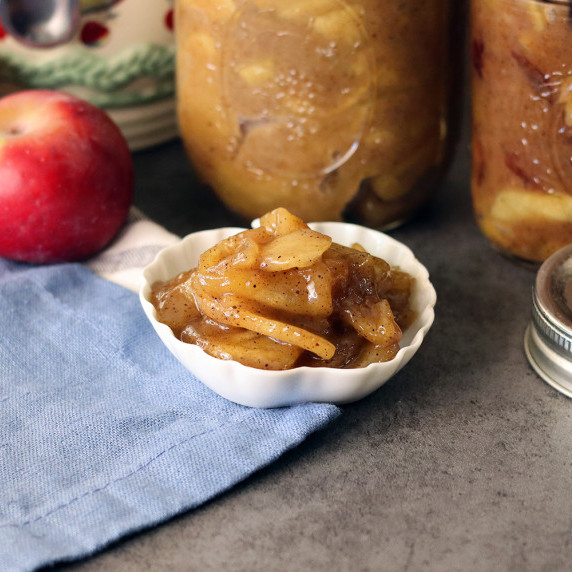 Jars of caramel apple pie filling with a small dish of caramel apple pie filling in front