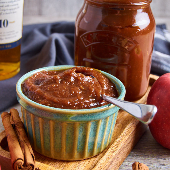 A jar and small ramekin filled with Pressure Cooker Apple Butter with Malt. Surrounded by apples.