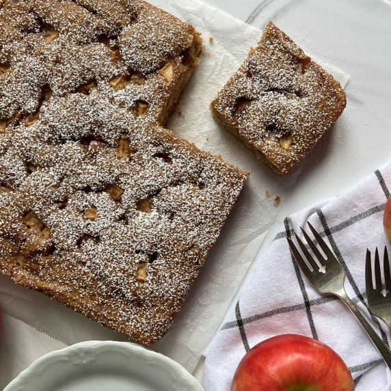 Apple cake dusted with powdered sugar on parchment paper.