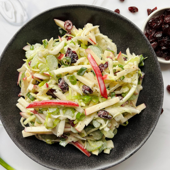 Coleslaw with sliced apples in a gray bowl on a white background.