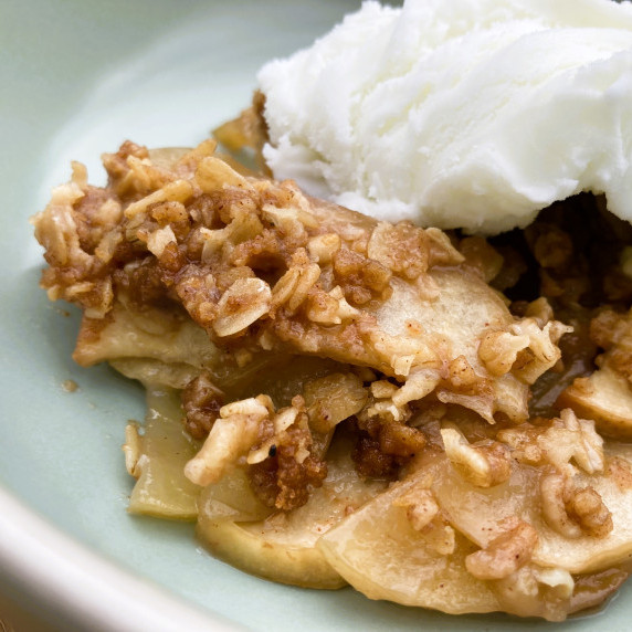 Scoop of apple crisp topped with vanilla ice cream in a blue bowl.