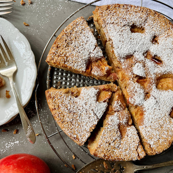 Sliced apple cake on a wire rack topped with powdered sugar.