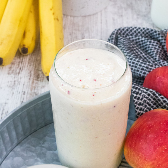 Apple and banana smoothie in glass surrounded by fruit