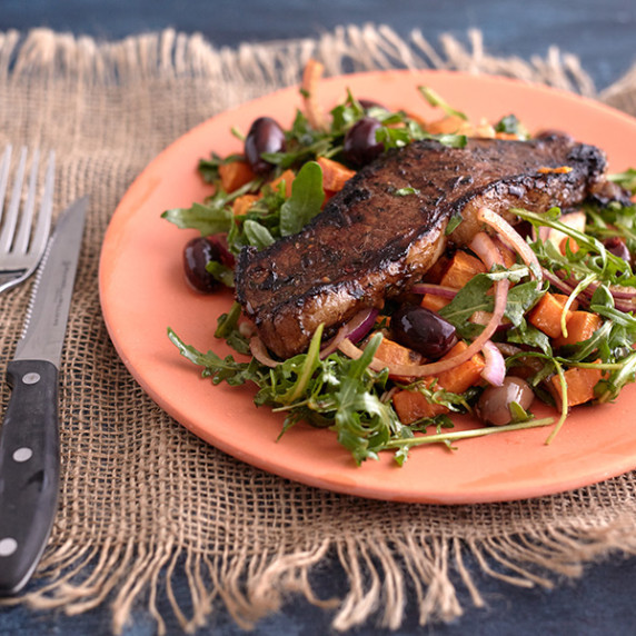Juicy steak on bed of arugula salad with cubes of sweet potatoes, olives and red onion on a plate