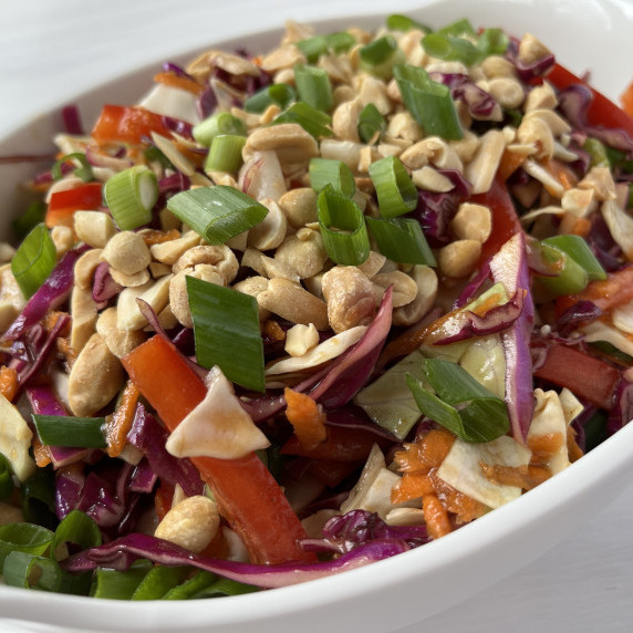 Cabbage, red peppers, carrots, scallions, and peanuts tossed in a savory dressing in a white bowl.