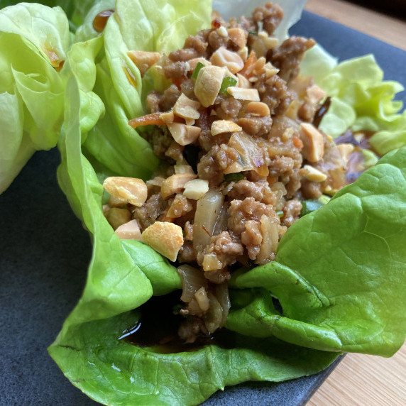 Bibb lettuce leaf filled with seasoned ground turkey drizzled with a brown sauce on a black plate.