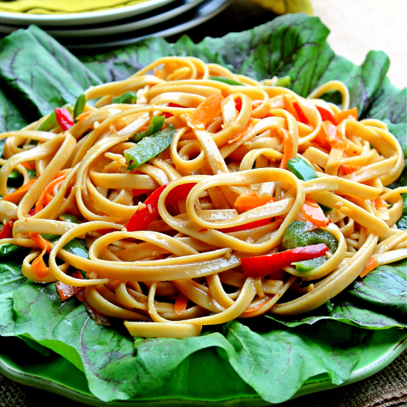 Linguini noodles, carrots, green and red peppers with an Asian sauce on a bed of lettuce