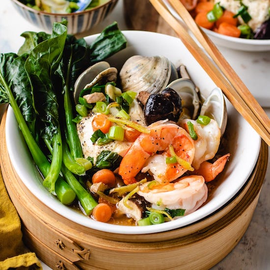 Shrimp, clams, bok choy, green onions in a basket steamer with chopsticks