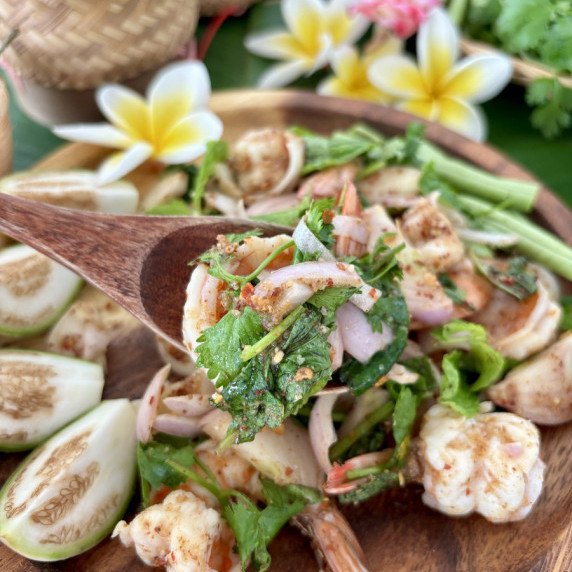 Close-up of shrimp larb salad, with a fork lifting a forkful of shrimp and fresh herbs.
