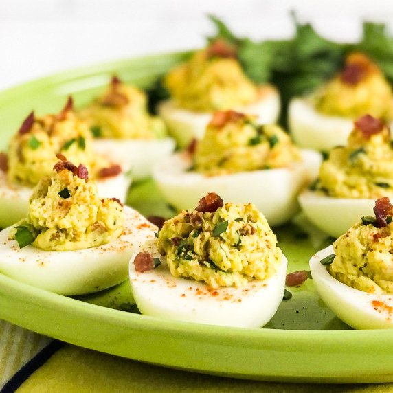 Avocado Deviled Eggs on a green plate garnished with chives and bacon.