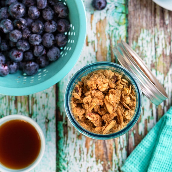 A jar of granola on a wooden table next to blueberries and coffee.