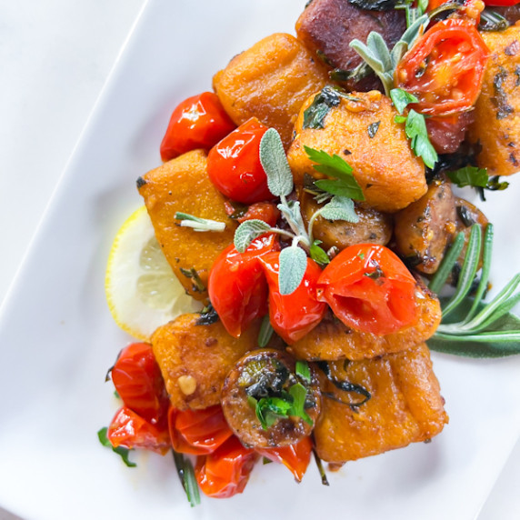 Sweet potato gnocchi on a plate with tomatoes and rosemary leaves.