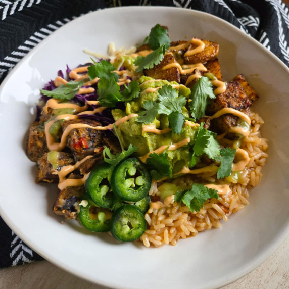 A white bowl filled with colourful components, green garnishes, and a black towel in the background.