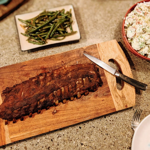 barbecue pork ribs on a wooden board with a side of potato salad and green beans