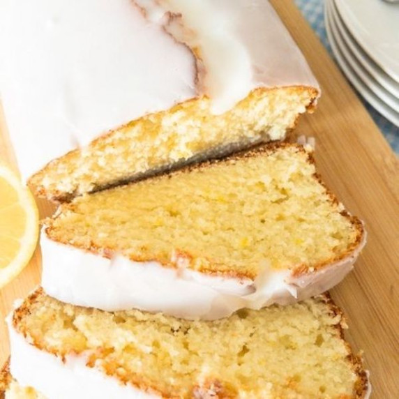 Iced lemon loaf on a wooden cutting board with two slices cut out of it.