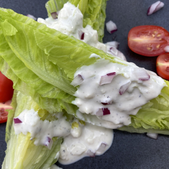 Romaine lettuce wedges with blue cheese dressing, diced red onion and tomatoes on a gray plate.